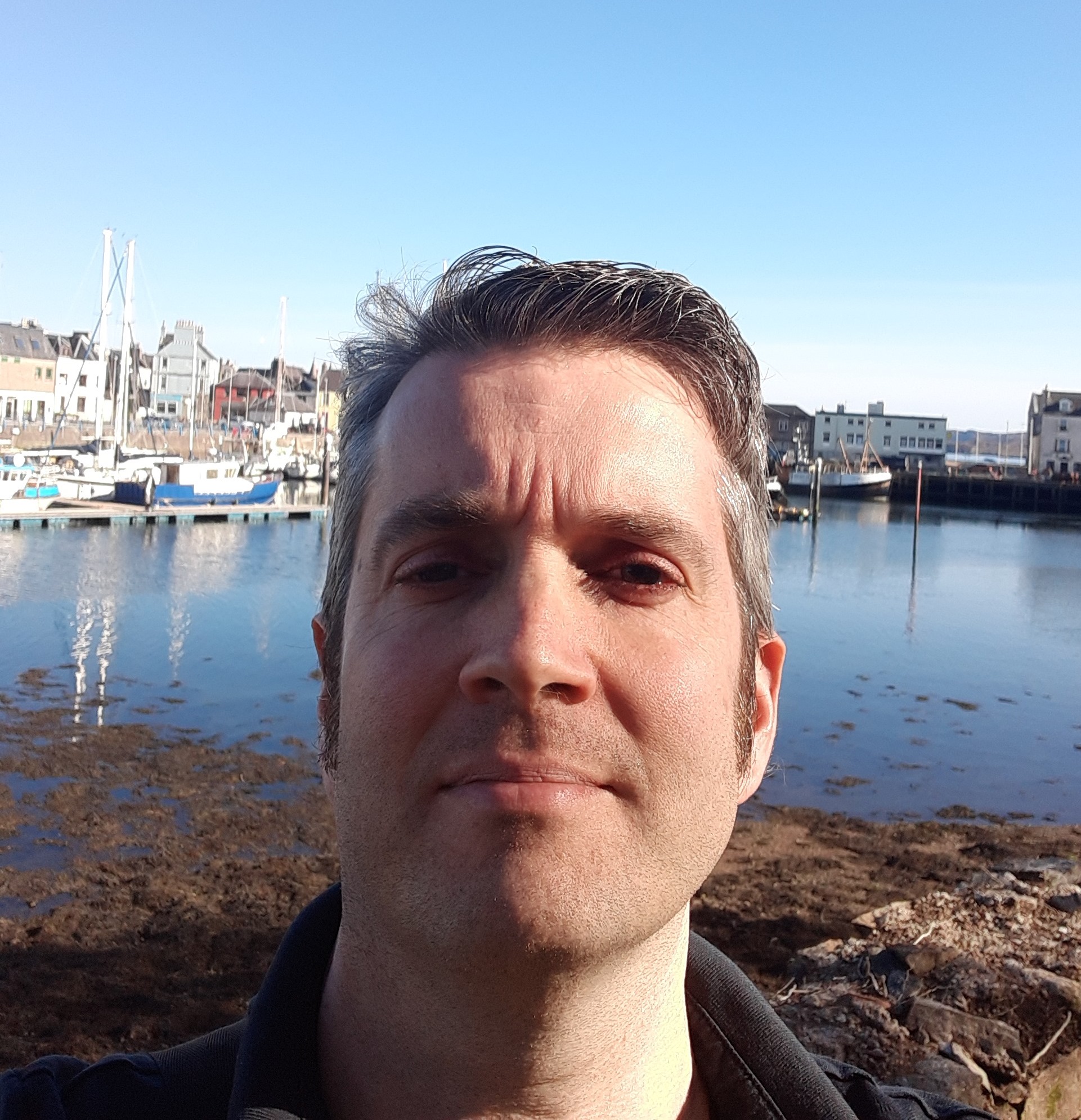 Image shows a headshot of Dave infront of the harbour at Stornoway