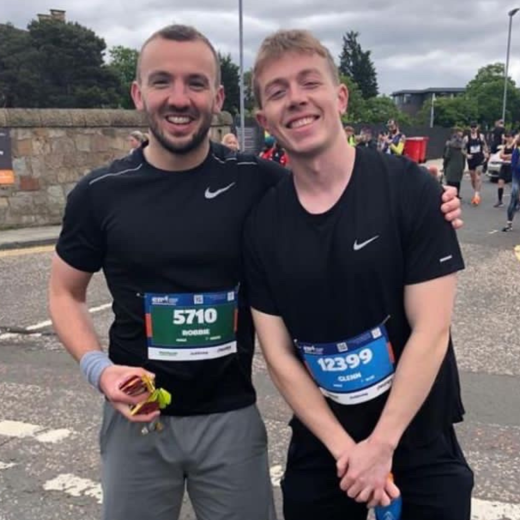Image shows Robbie and Glenn standing beside each other after finishing the Edinburgh marathon, smiling to camera despite the sore legs.