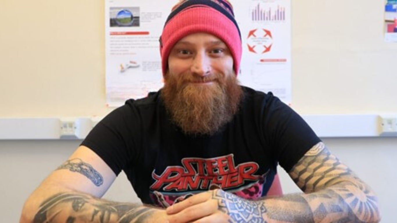 Image shows steve smiling to camera showing some rather fabulous tattoos and wearing his trademark beanie hat
