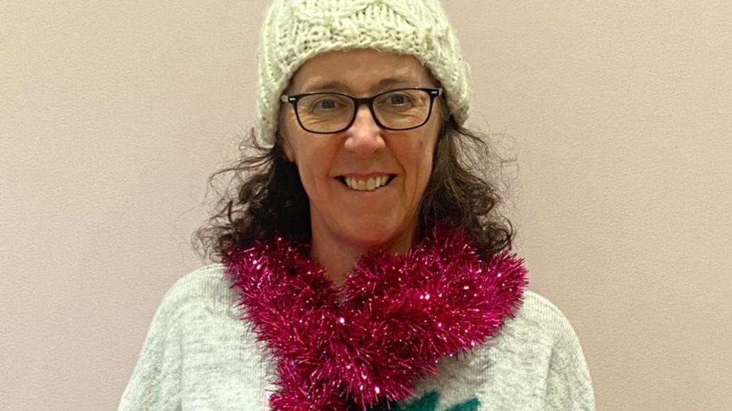 image shows sheena smiling to camera wearing her fashion forward winter hat and jumper, adorned by her red tinsel