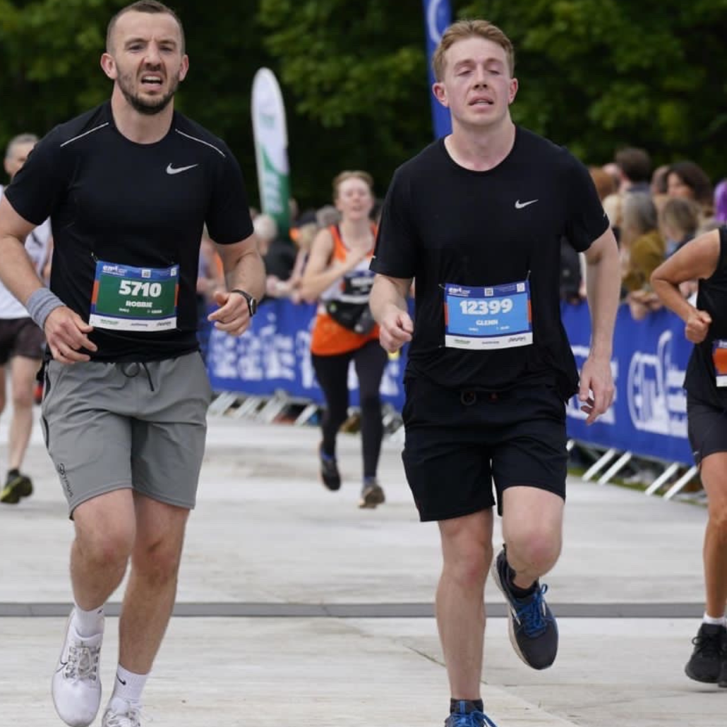 Image shows Robbie and Glenn running during the Edinburgh marathon. They're running beside each other wearing a mix of black and grey running shorts and t-shirts.
