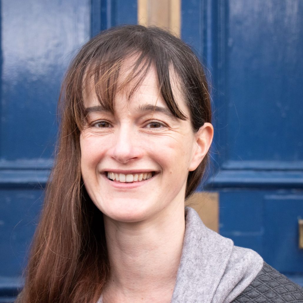 Image shows a head and shoulders shot of Sarah against the background of a dark blue door